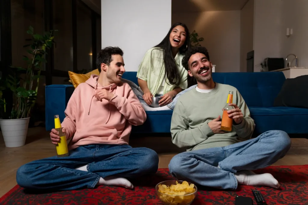 Jeunes amis riant devant la télévision en profitant d'un test IPTV gratuit avec boissons et chips